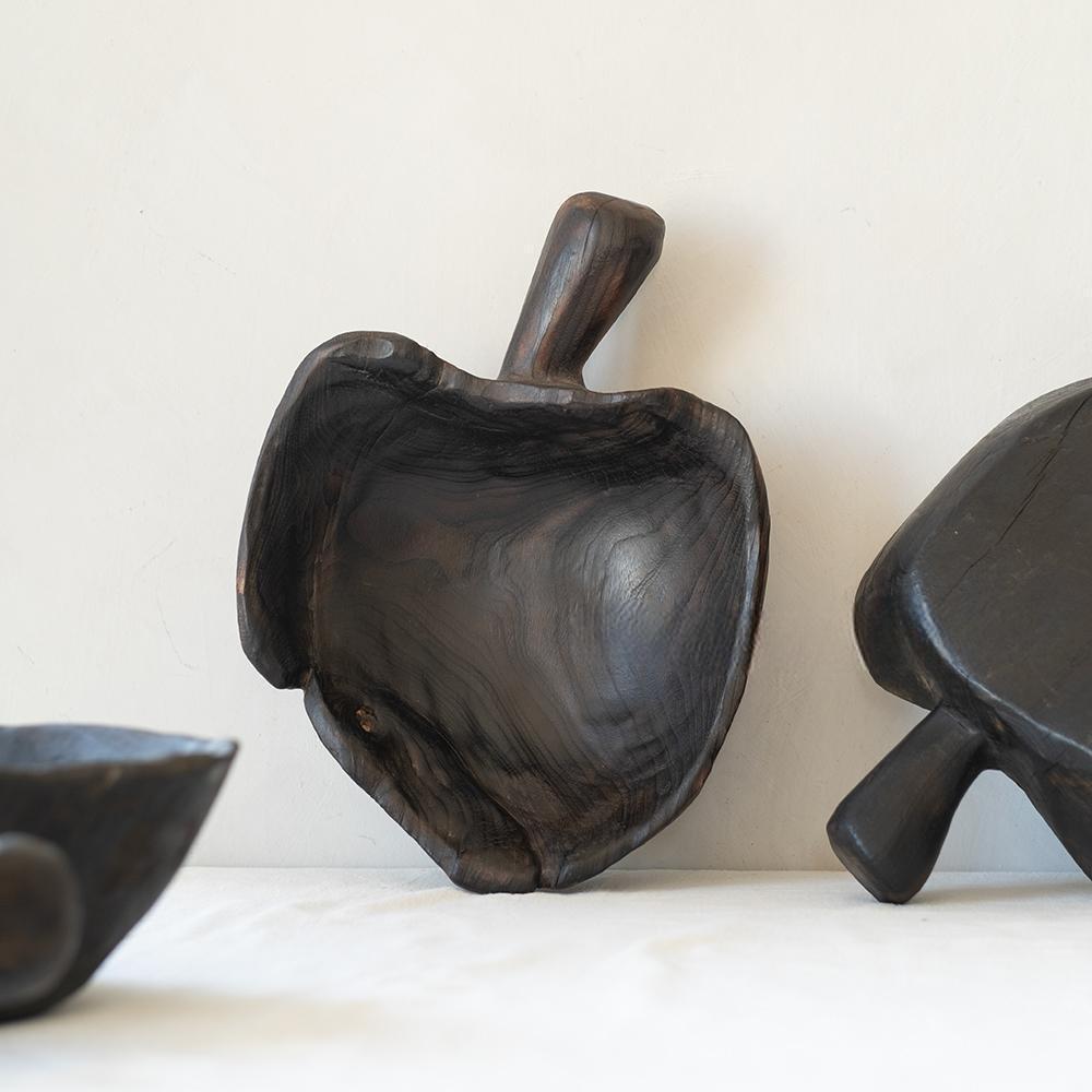The Camphor Wood Fruit Handled Tray, Home (14 x 9 x 11 in), with its apple shape and short handle, rests against a light background alongside partial views of similar wooden items.