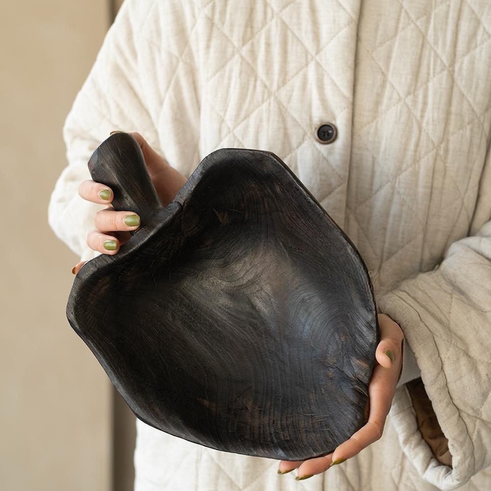 A person with light green nail polish holds a Camphor Wood Fruit Handled Tray, Home (14 x 9 x 11 in), wearing a cream-colored quilted jacket.