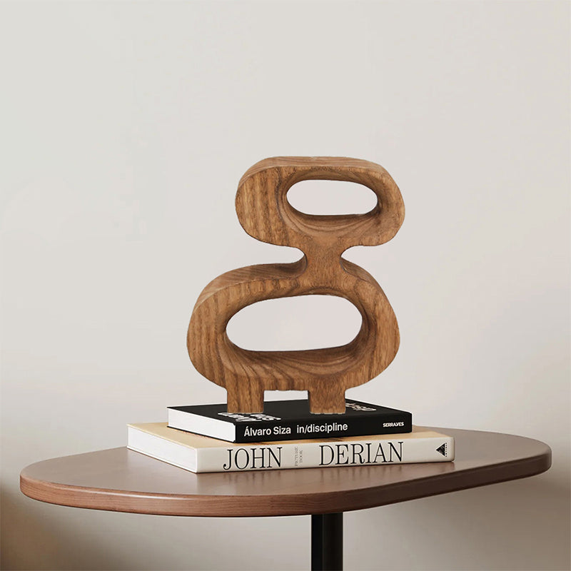 The Geometric Solid Wood Wall Sculpture, Living Room hangs above two stacked books on a small curved wooden table, forming a minimalist scene that evokes the feel of abstract modern art against a plain, light-colored wall.