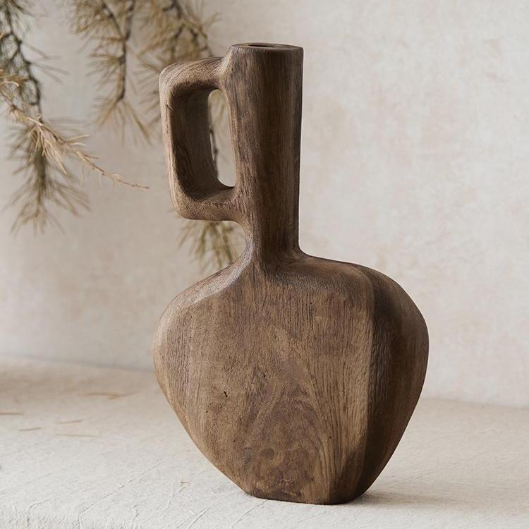 The Tall Solid Wood Vase (8×2.4×12.6 in) features an asymmetrical, organic design with a striking handle—ideal for rustic home decor and stunning when displayed with dried branches on any textured surface.