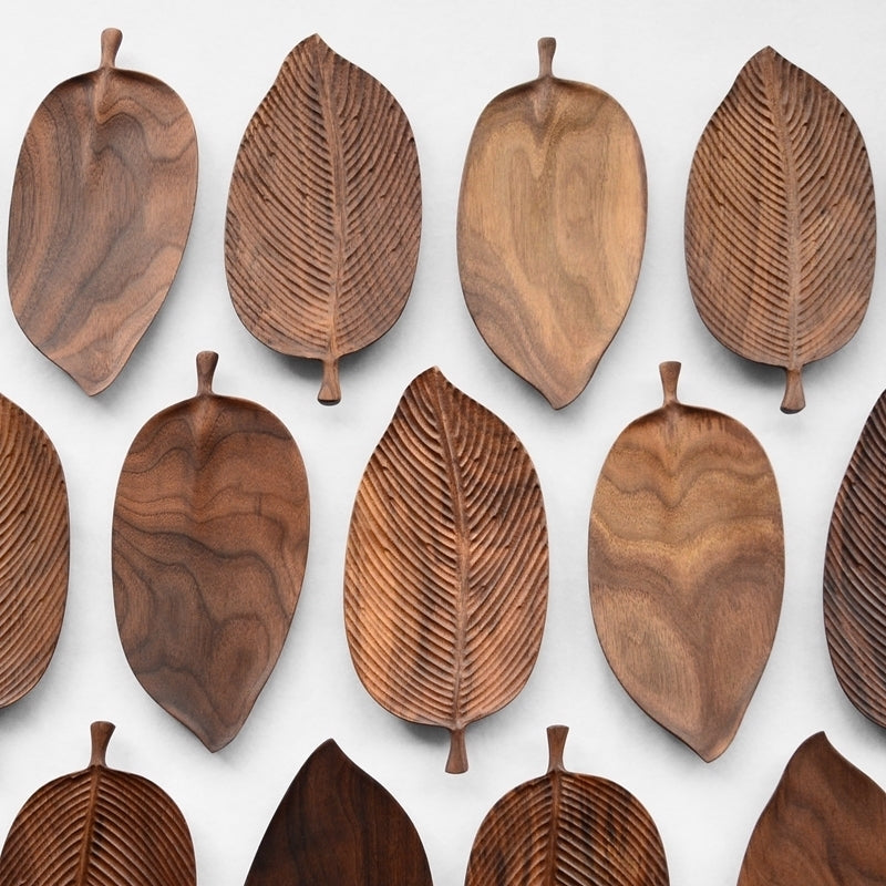 Leaf-Shaped Black Walnut/Rubberwood Serving Trays are arranged in neat rows on a white background. Each tray features carved vein patterns, a small stem-like handle, and unique natural wood tones and grain patterns.