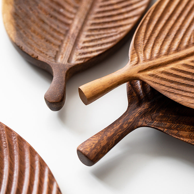 Close-up of several Leaf-Shaped Black Walnut/Rubberwood Serving Trays, showcasing intricate vein patterns and elongated stems, beautifully arranged on a white surface—ideal for adding Japanese-inspired style to any space.